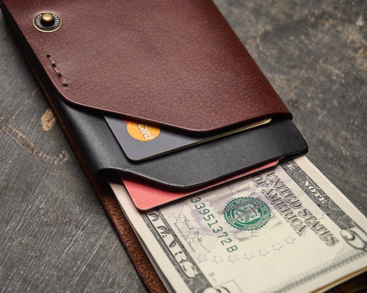 Close-up of a two-tone brown and black hand-stitched leather envelope wallet holding credit cards and folded bills.