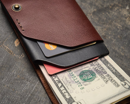 Close-up of a two-tone brown and black hand-stitched leather envelope wallet holding credit cards and folded bills.