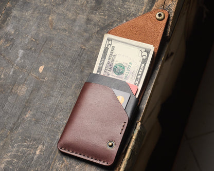 Open slim leather cash wrap wallet on a wooden desk, displaying interior black card slots filled with cards and folded five-dollar bills.
