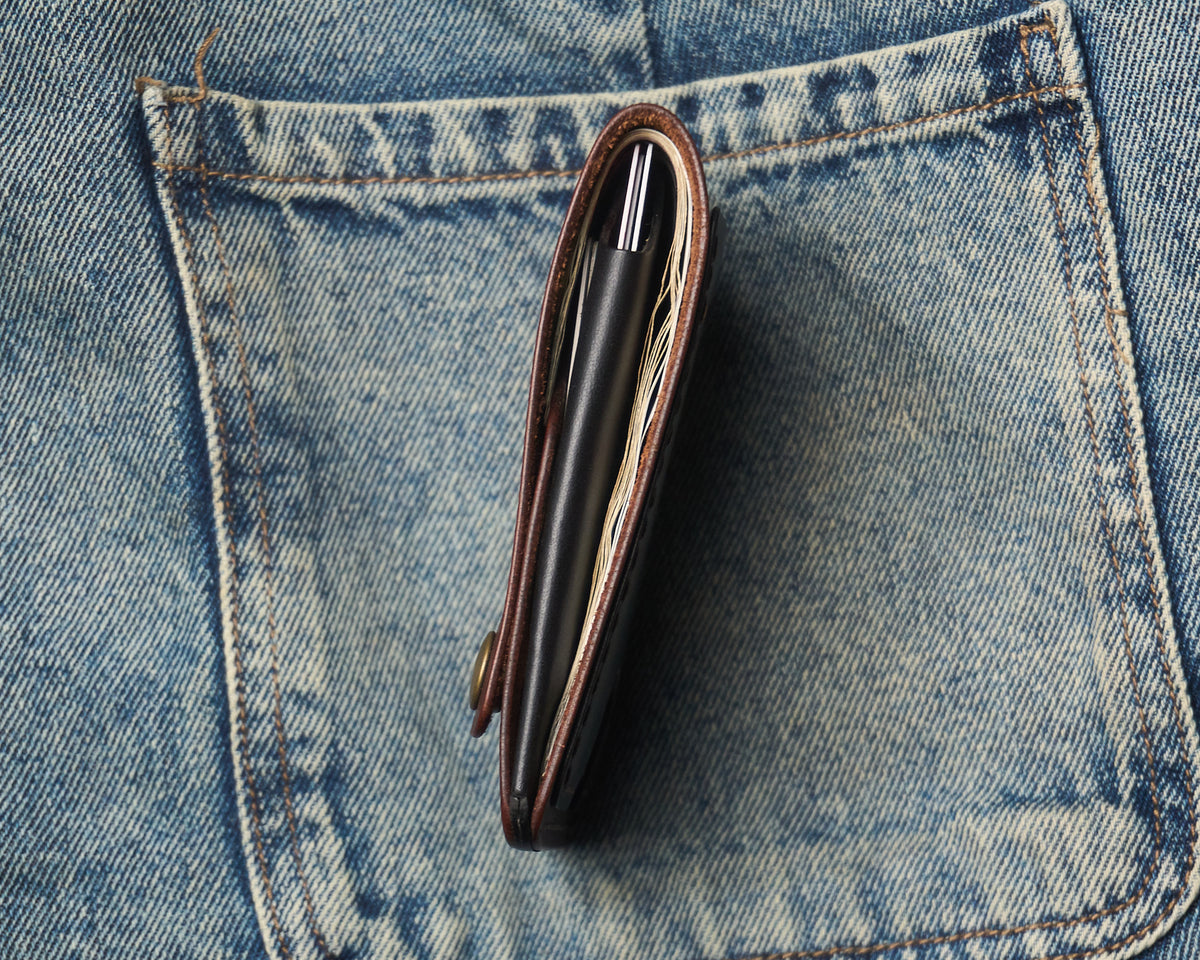 Side profile of a slim everyday carry (EDC) leather wallet filled with cards and cash, demonstrating its thin profile inside a denim jeans pocket.
