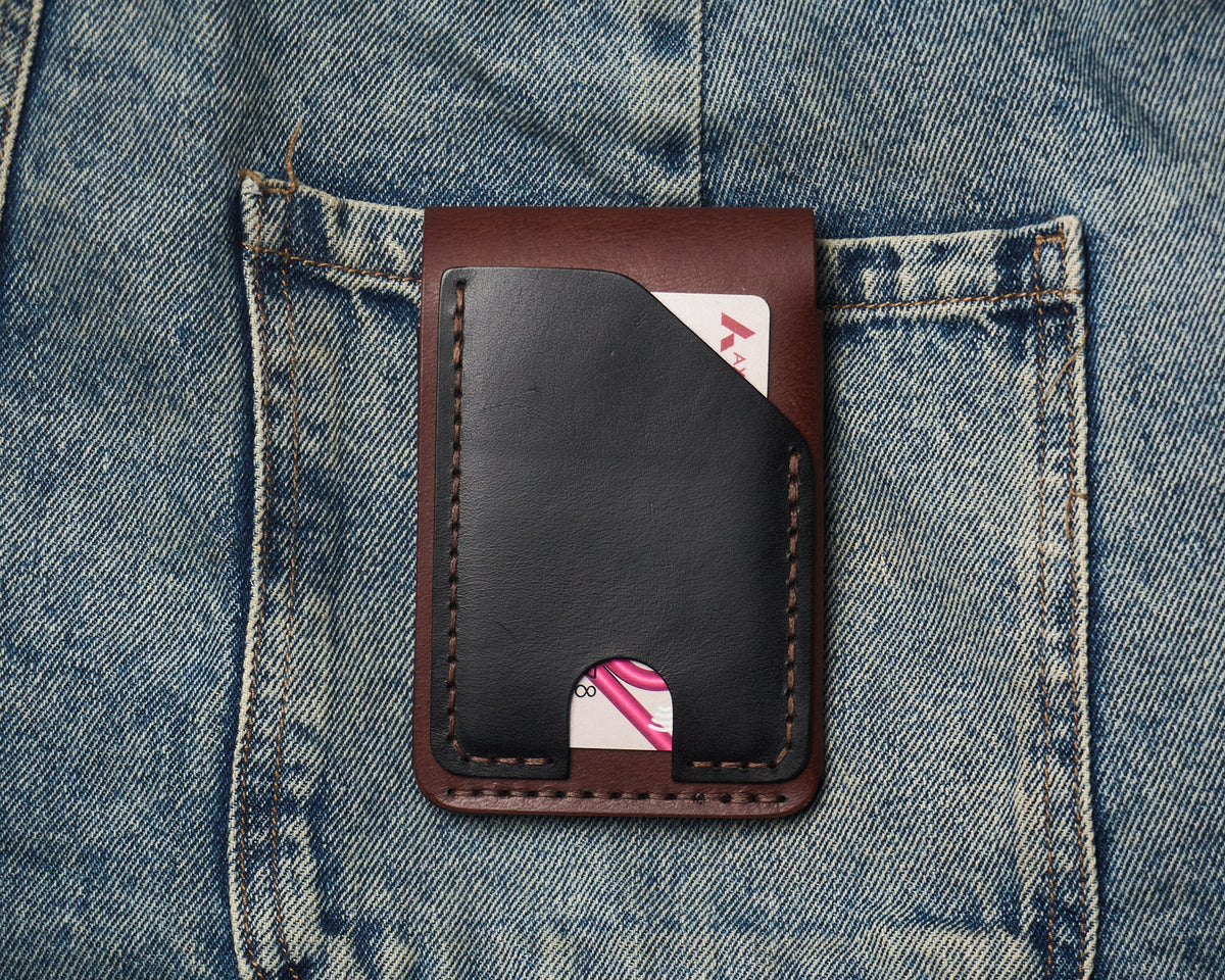 Back view of a two-tone leather wallet resting on blue jeans, featuring a quick-access black leather card slot with hand-stitched detailing.