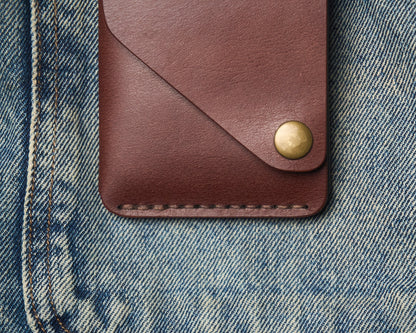 Close-up of a handcrafted leather wallet on denim, highlighting the thick hand-stitched thread, brass snap hardware, and rich brown leather grain